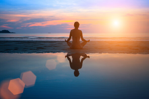 Silhouette young woman practicing yoga on the beach at sunset