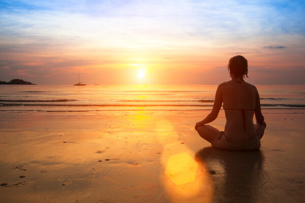 Woman practicing yoga on the ocean beach at sunset.