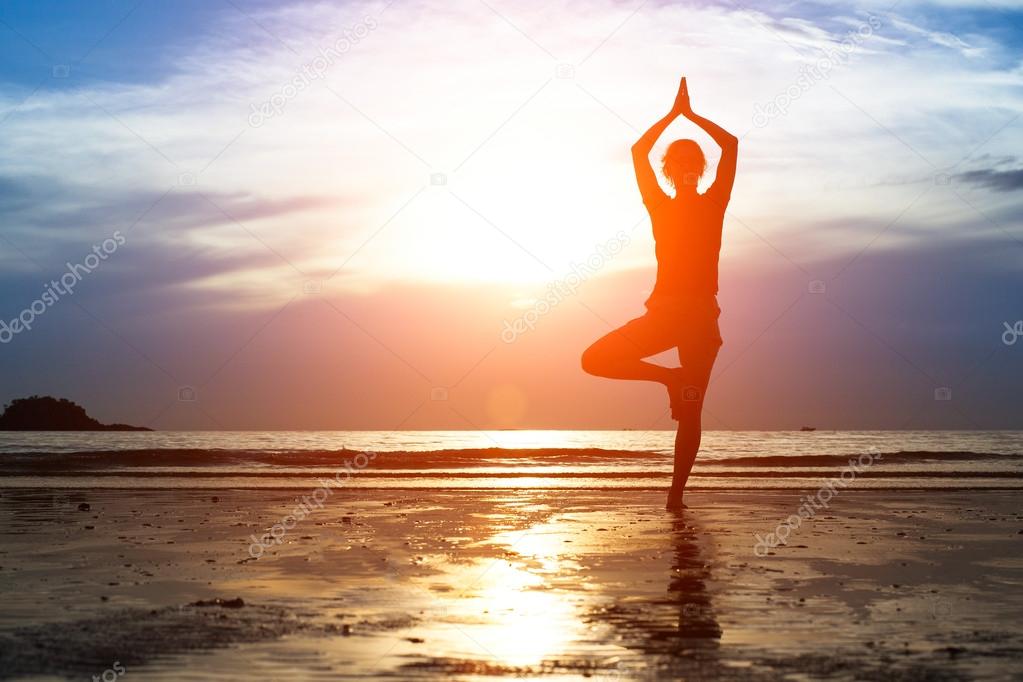 Silhouette woman practicing yoga on the beach at sunset.