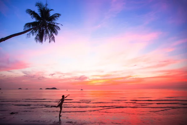 Sziluettjét fiatal nő egy ugrás a tengerre tengerparton napnyugtakor (koncepció a vágyódik-vár szünidő) — Stock Fotó