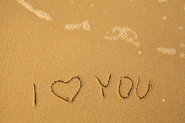 Jag älskar dig - text skriven för hand i sand på en strand med en blå våg. — Stockfoto