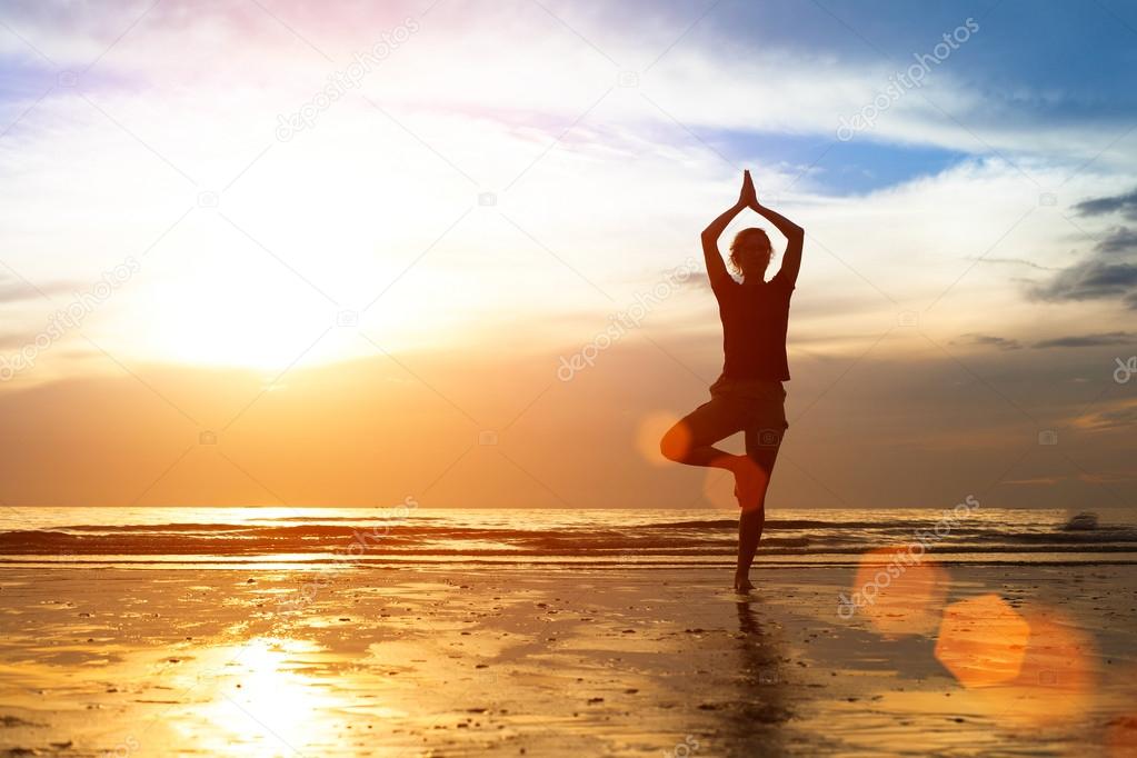 Silhouette of a young woman practicing yoga at sunset.