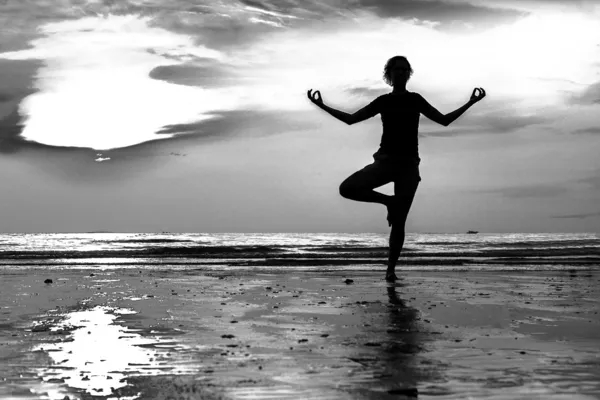 Junge Frau praktiziert Yoga am Strand bei Sonnenuntergang (Schwarz-Weiß-Foto)) — Stockfoto