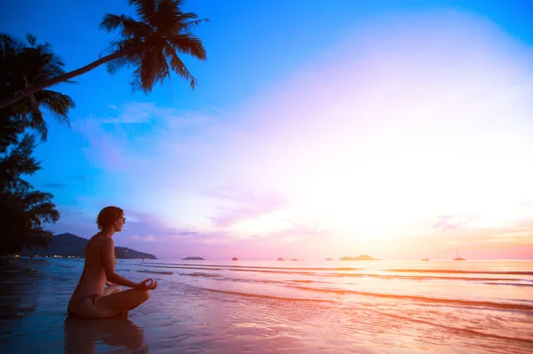 Gün batımında plajda yoga yapan genç bir kadın. — Stok fotoğraf