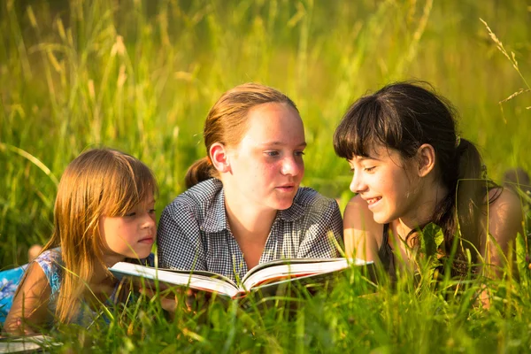 Three little sister reading book in natural environment together — Stock Photo, Image