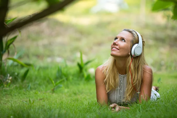 Mooi emotionele meisje met koptelefoon in het park op zonnige dag. — Stockfoto