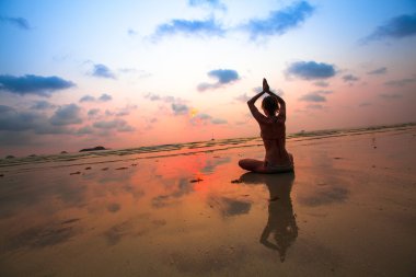 Deniz günbatımı üzerinde bir kadın yoga silüeti.