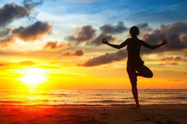 Mladá žena cvičí jógu na pláži při západu slunce — Stock fotografie