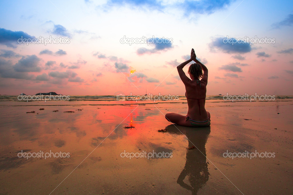 Yoga woman sitting on sea coast at sunset