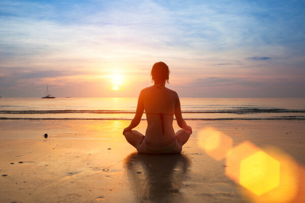 Silhouette young woman practicing yoga on the beach at sunset