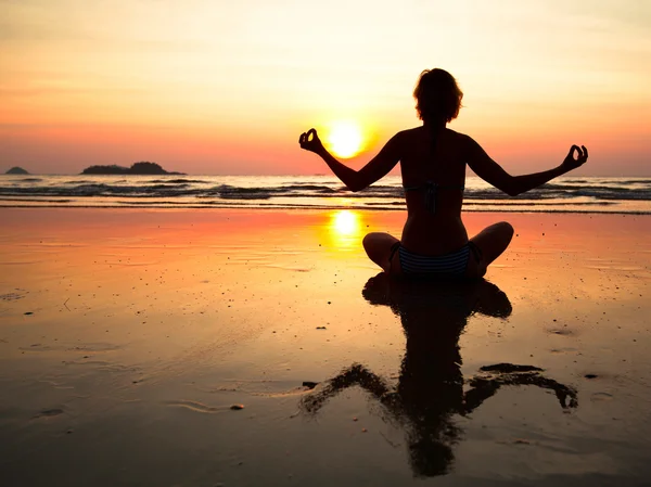 Mujer de yoga joven sentada en la costa del mar al atardecer — Foto de Stock