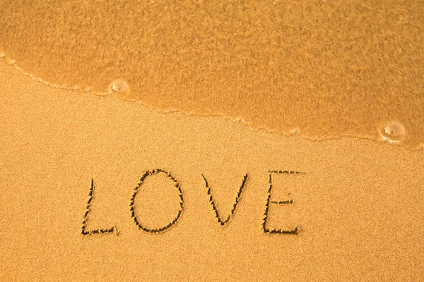 Liefde - geschreven door hand in zand op een strand, met een zachte Golf — Stockfoto