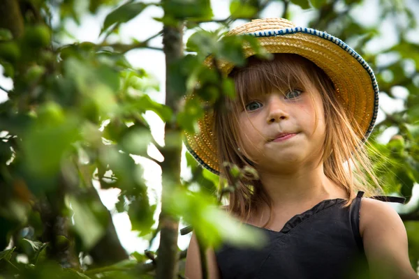 Kleines hübsches Mädchen posiert mit Strohhut im Park — Stockfoto