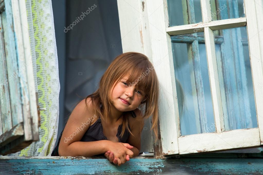 Little girl looks out the window rural house.
