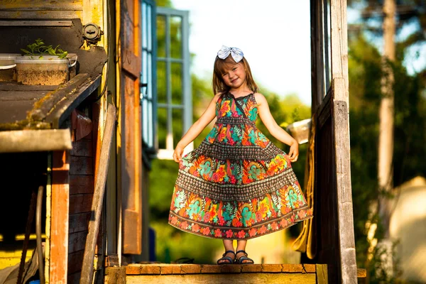 Linda menina de cinco anos posando para a câmera no alpendre de uma casa de aldeia ao pôr do sol — Fotografia de Stock