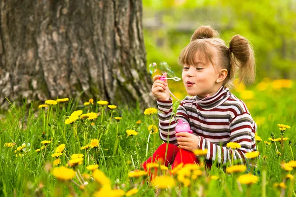 Смішна п'ятирічна дівчина дме мильні бульбашки в парку Стокова Картинка