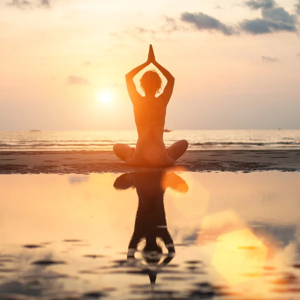 Mujer de yoga sentada en posición de loto en la playa al atardecer —  Fotos de Stock