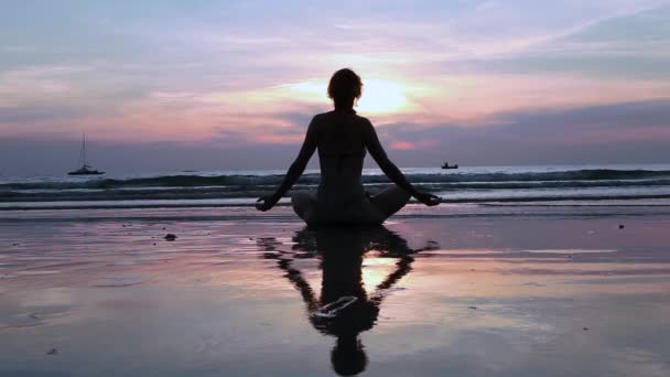 Silhouette ung kvinna utövar yoga på stranden vid solnedgången. — Stockvideo