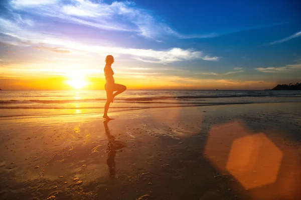 Silhouet van een jonge vrouw doen oefeningen bij zonsondergang op de kust. — Stockfoto