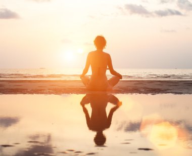 yoga kadın Lotus poz sahilde günbatımı sırasında oturuyordu.