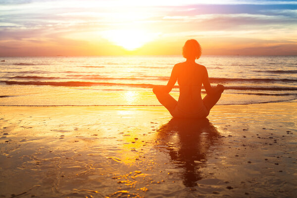 Silhouette of woman practicing yoga on the beach