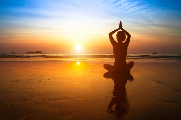 Yoga woman sitting on sea coast at sunset.