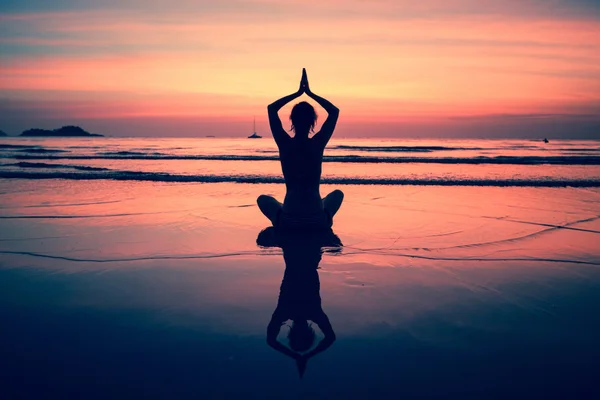 Mujer de yoga sentada en la costa del mar al atardecer . — Foto de Stock