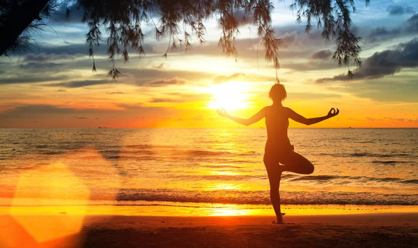 Yoga vrouw aan de kust van de zee bij zonsondergang. — Stockfoto