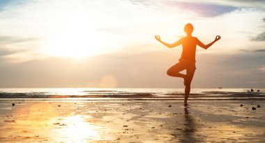 Gün batımında kumsalda yoga yapan kadın.