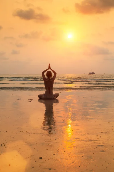 Jovem praticando ioga na praia ao pôr do sol — Fotografia de Stock