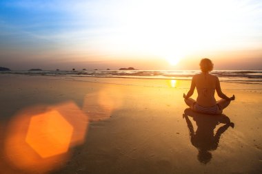 Gün batımında sahilde meditasyon yapan bir kadın..
