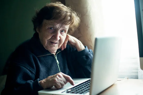 An old woman is study typing on a laptop at her home.