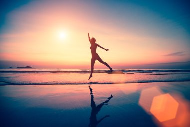vrouw springen op het strand bij zonsondergang.