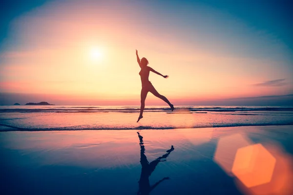 Vrouw springen op het strand bij zonsondergang. — Stockfoto