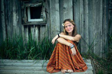 Hippi elbiseli genç kız dışarıda köyde oturuyor..
