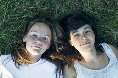 Çimlerin üzerinde yatan iki genç kızın portresi, yukarıdan yakından çekilmiş..