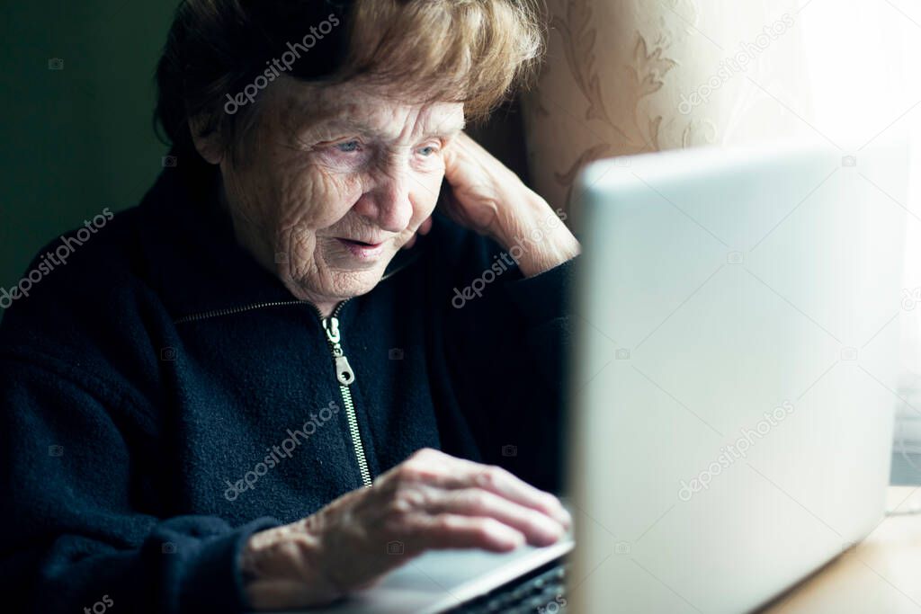 An old woman working on the computer in her home.