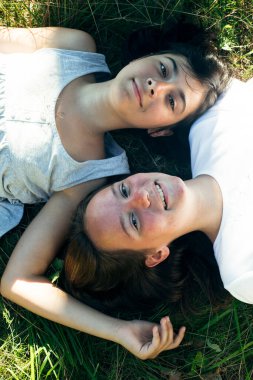 İki genç kızın portresi bir yaz parkında yeşil çimlerin üzerinde yatıyor..