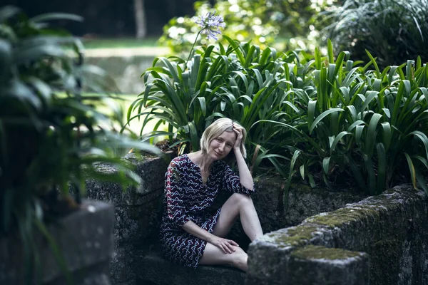 Portekiz, Porto 'daki eski bir parkta, yeşil alanların arasında taş bir bankta oturan bir kadın..