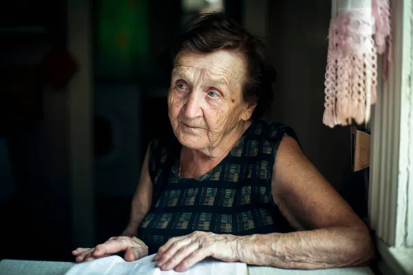 一位老妇人坐在家里的厨房里看书 — 图库照片