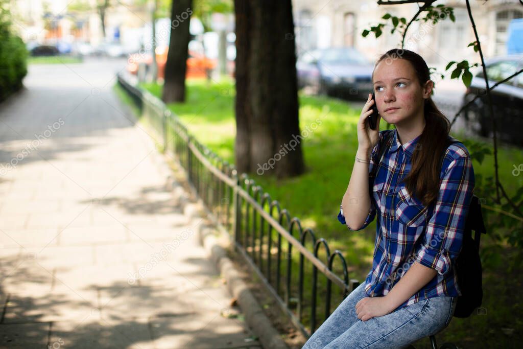 A teenage girl is talking on her cell phone while sitting in the square.