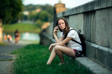 Parkta otururken cep telefonuyla konuşan bir kız..