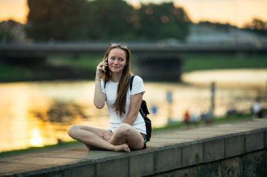 Şehrin rıhtımında otururken cep telefonuyla konuşan tatlı bir kız..