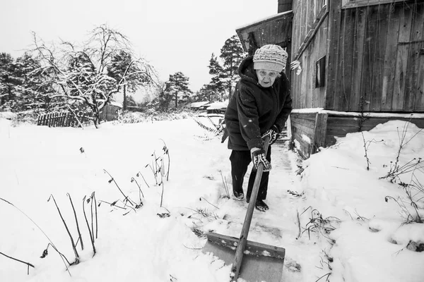 老人は田舎の家の外で雪を掘っている 白黒写真 ストックフォト