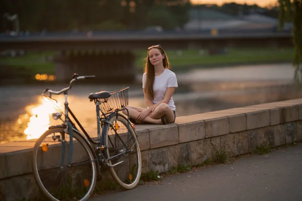 Een Meisje Met Een Fiets Zittend Aan Stadswaterkant Bij Zonsondergang Rechtenvrije Stockfoto's
