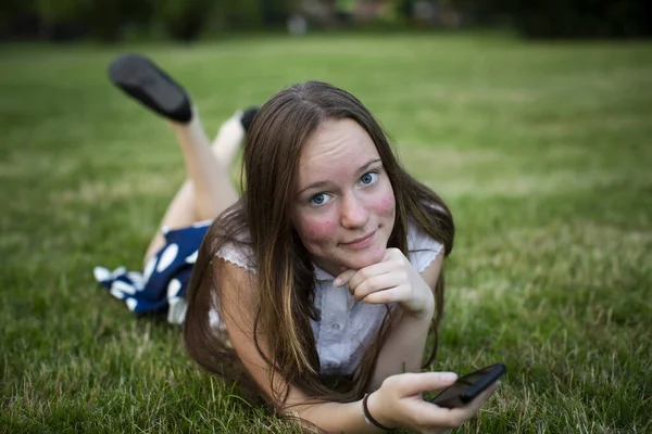 一个拿着智能手机的女孩躺在绿草中 — 图库照片