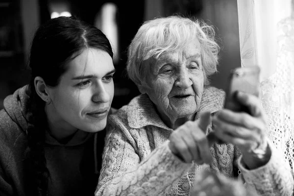 一位老妇人和他的成年孙女一起看他的智能手机 黑白照片 — 图库照片