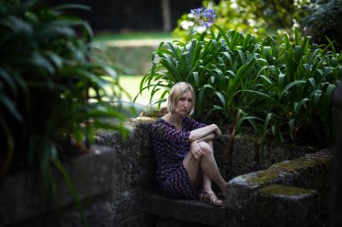 A young woman sitting on a stone bench in an ancient Portuguese park. 