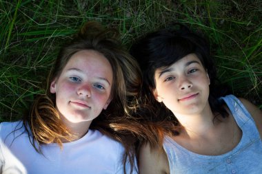 Portraite of two teenage girl lying on grass and having good time. 