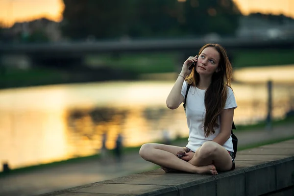 Дівчина Говорить Телефону Сидячи Набережній Міста Під Час Заходу Сонця — стокове фото
